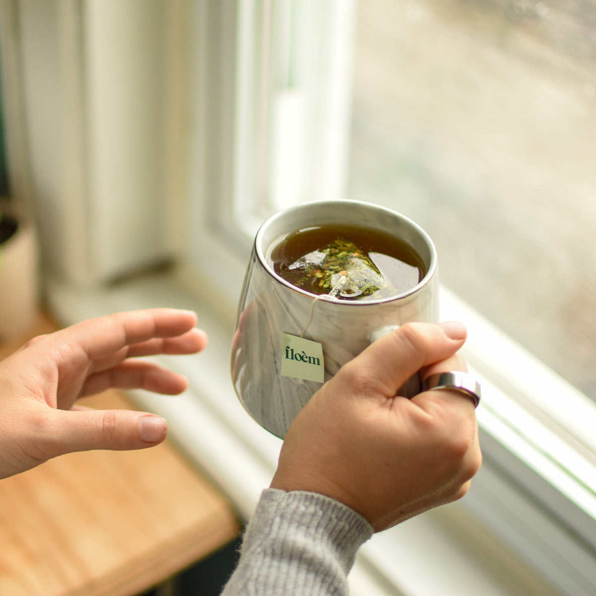Sachet de thé Floèm dans une tasse devant une fenêtre